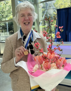 Dr. Wendie Berg and her SBI Gold Medal on stage with flowers.